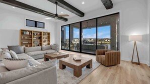 A modern living room with a sofa, coffee table, and armchair, a wooden bookshelf, and a large sliding glass door leading to an outdoor area. - Ellen Lake Luxe | Concierge Services (Kingsland)