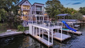 A waterfront property with a multi-level deck, a blue slide, and a covered area with a roof. - Ellen Lake Luxe | Concierge Services (Kingsland)