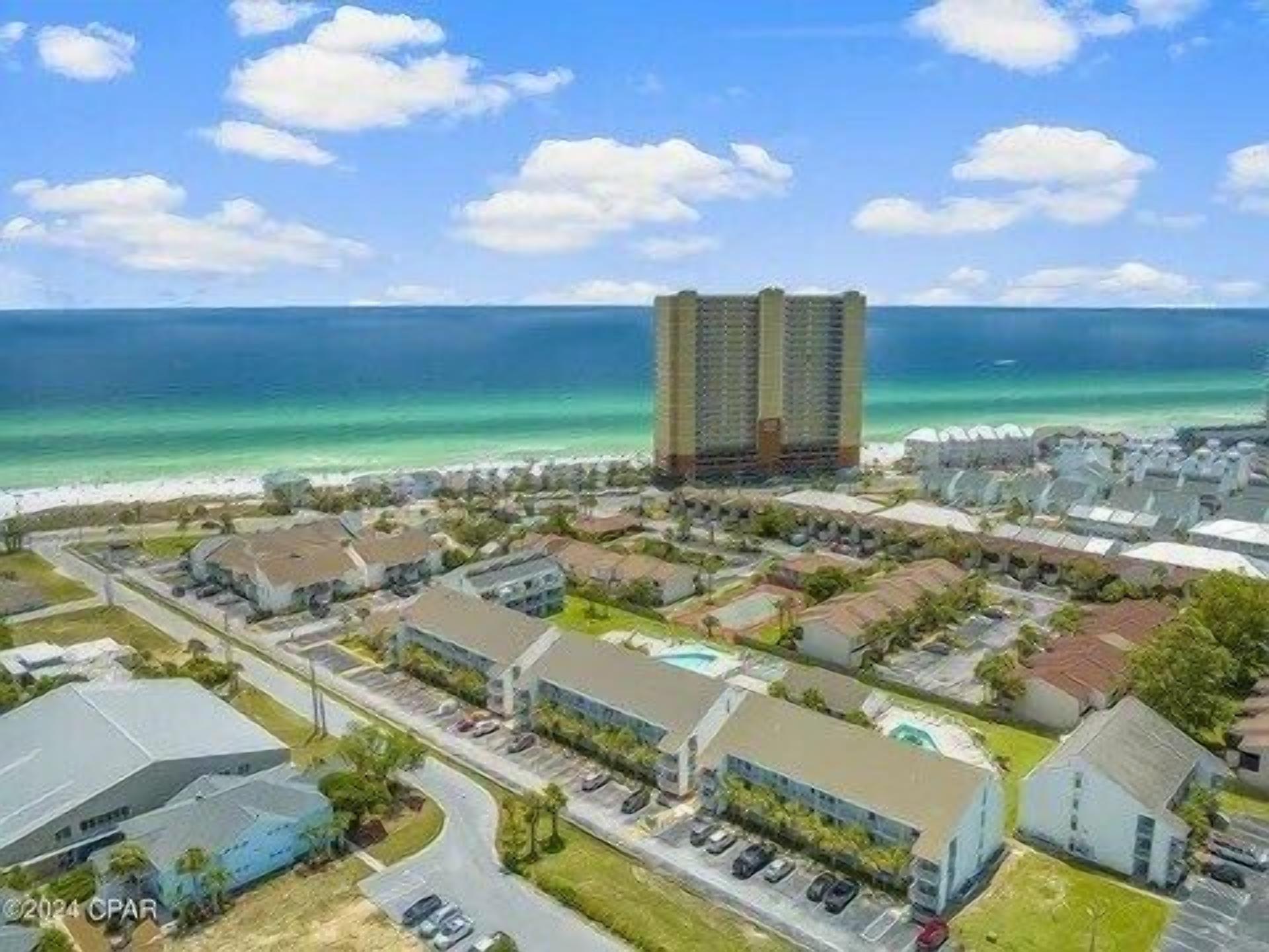 A coastal residential area with a prominent high-rise hotel, a marina, and a beach.