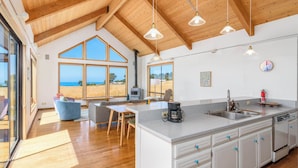 A spacious kitchen with a large island, wooden ceiling beams, and large windows offering a view of the sea. - Spacious 3 BD for 6 + Ocean View (Sea Ranch)