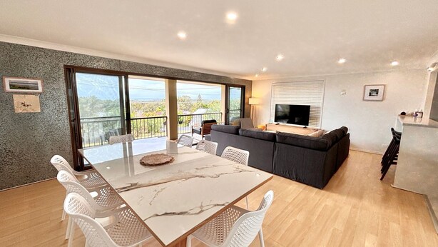 Ein modernes Wohnzimmer mit Essbereich, einer Sofagarnitur, einem Fernseher und einem Balkon mit Blick.