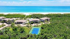 Ein Resort mit mehreren Gebäuden, einem Tennisplatz und Blick auf den Strand.