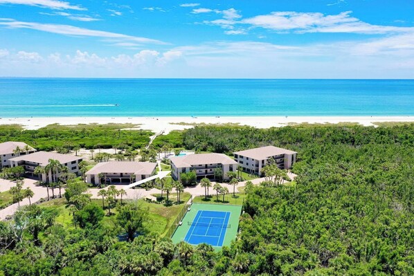 A resort with multiple buildings, a tennis court, and a beach view.