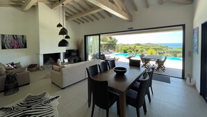 A spacious living area with a dining table, sofa, and a view of a swimming pool and hills. - Luxury villa in private estate with sea view and beach access 150 metres away (Zonza Sainte Lucie de Porto Vecchio)