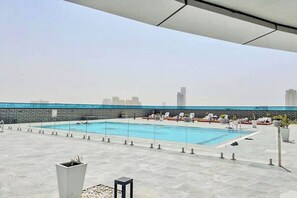 A rooftop pool with lounge chairs and a city skyline in the background.