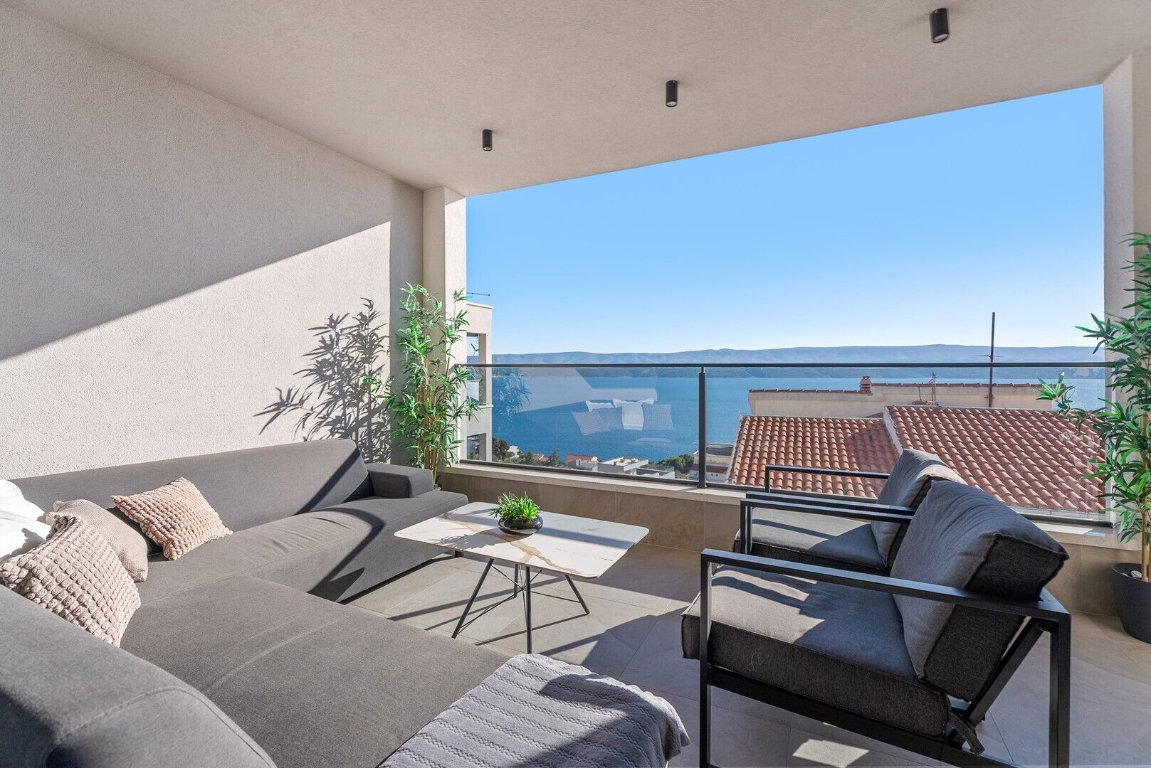 Ein Balkon mit einer Couch, Stühlen und einem kleinen Tisch mit Blick auf die Küste.