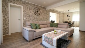 A modern living room with a beige sofa, a coffee table with a floral table runner, and a stone wall with a clock. - Beautiful Casa Nerlović with swimming pool (Vrvari)