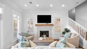 A living room with a fireplace, two sofas, a coffee table, and a TV mounted on the wall.