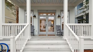 A white wooden porch with a double door, two black wall lamps, and a bicycle parked to the left.