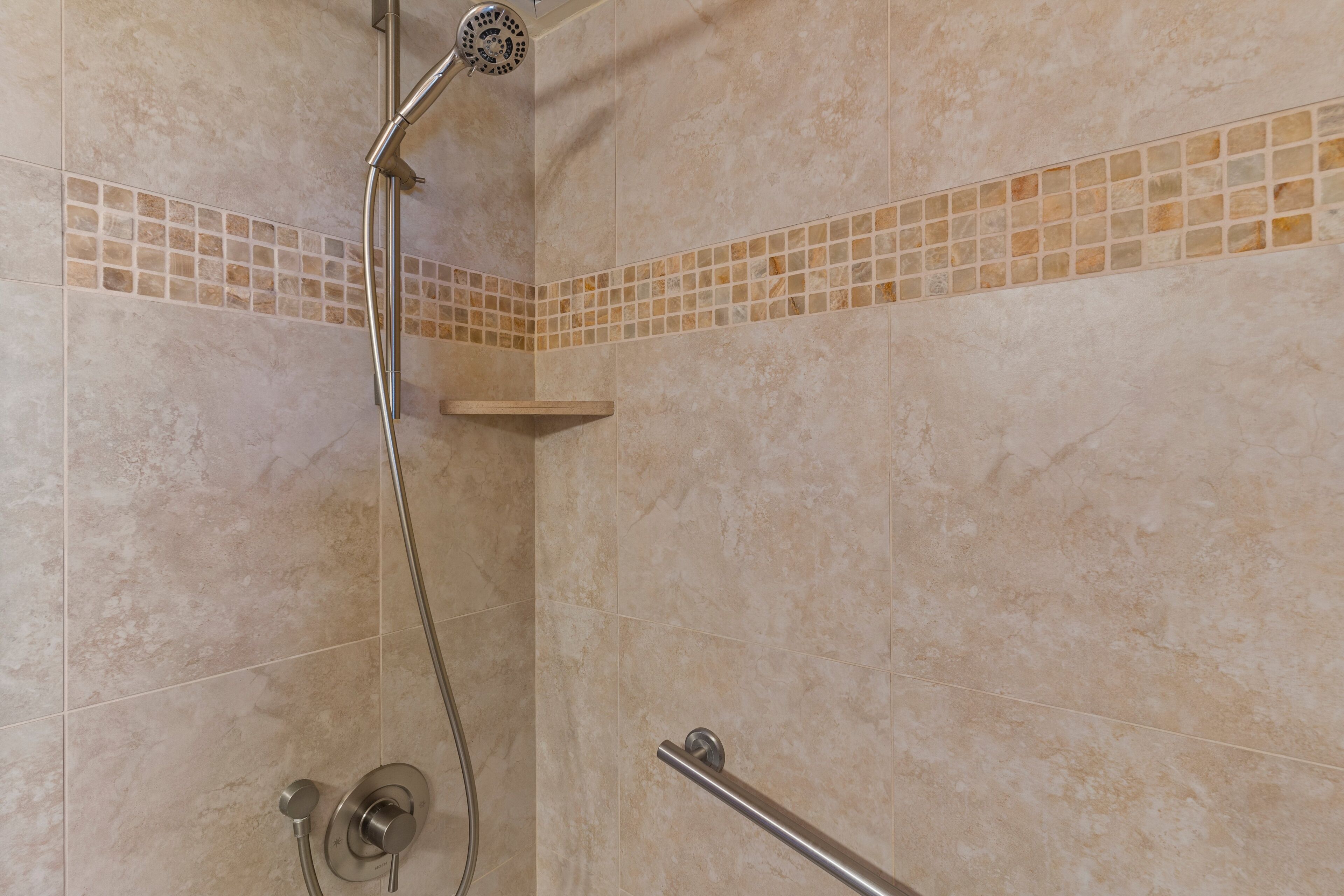 Ein Duschbereich mit Handbrause, Armaturen an der Wand und Ablagefläche in der Ecke.