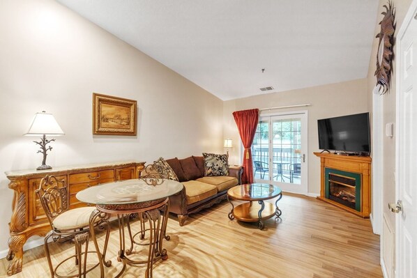 A living room with a sofa, a glass coffee table, a fireplace, a television, and a door leading to an outdoor area. - 3rd Floor Back Side Penthouse Suite - 306 by Grand Wood Suites (Nashville)