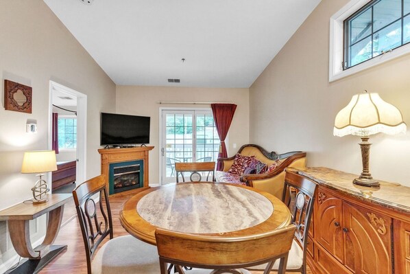 A dining area with a round table, chairs, a television, a fireplace, and a window with curtains. - 3rd Floor Back Side Corner Penthouse Suite- 305 by Grand Wood Suites (Nashville)