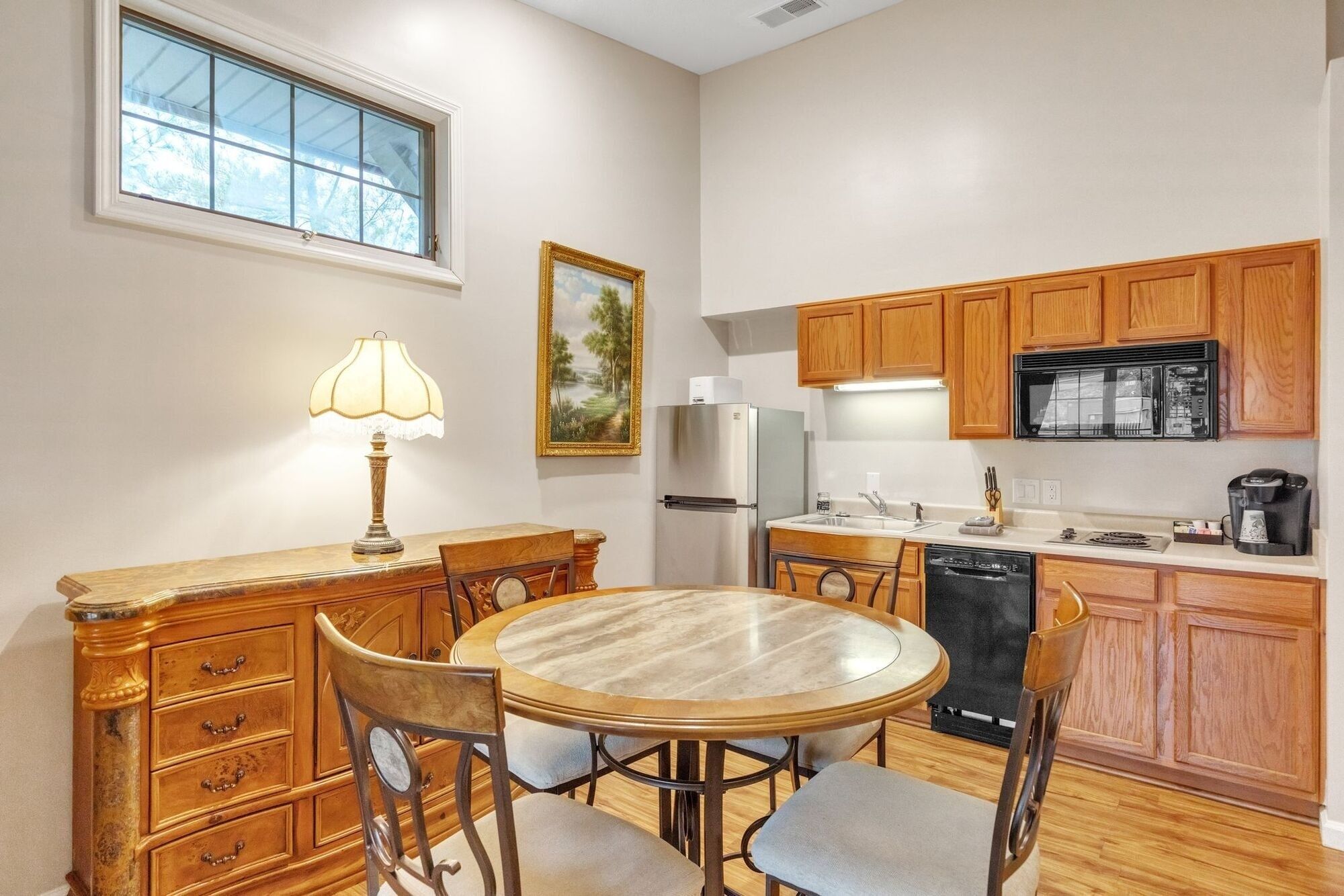 Cocina compacta con armarios de madera, un refrigerador, lavavajillas y comedor con mesa y sillas.