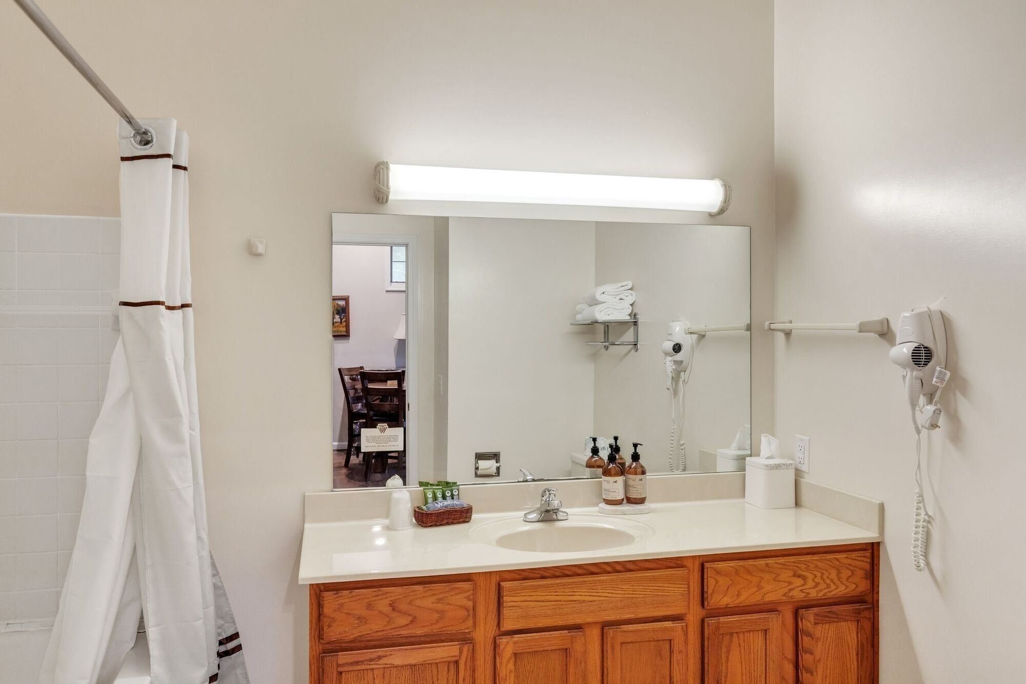 Une salle de bain avec un lavabo blanc, un meuble-lavabo en bois, un miroir, un porte-serviettes et un sèche-cheveux.