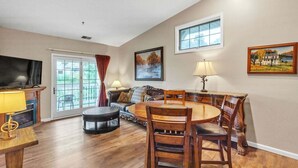 A spacious living room with a large TV, a dining table with chairs, a sofa, and a fireplace. - 3rd Floor Front Side Corner Penthouse Suite - 304 by Grand Wood Suites (Nashville)