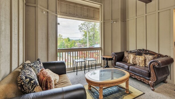 A room with a large window, a sofa, a coffee table, and a small table with chairs. - 3rd Floor Front Side Corner Penthouse Suite - 304 by Grand Wood Suites (Nashville)
