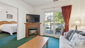 A hotel room with a bed, a TV, a fireplace, a sofa, and a balcony with a view of the outside. - 1st Floor Front Side Suite - 104 by Grand Wood Suites (Nashville)