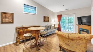 A living room with a wooden dining table, two chairs, a sofa, a TV, and a fireplace. - 3rd Floor Back Side Corner Penthouse Suite - 308 by Grand Wood Suites (Nashville)