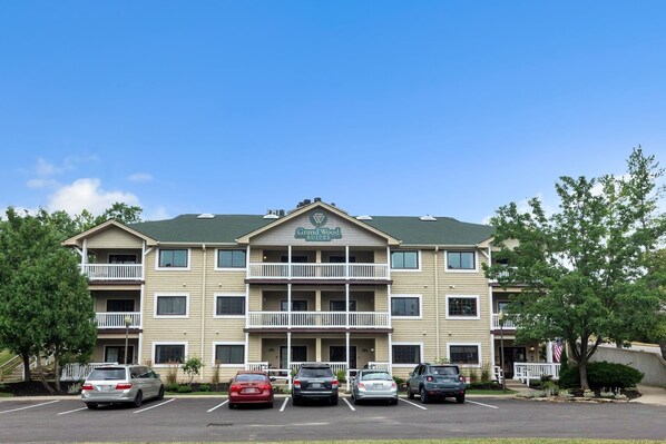 A multi-story hotel with a green roof, a balcony on the second floor, and a parking lot with several cars. - 3rd Floor Back Side Corner Penthouse Suite - 308 by Grand Wood Suites (Nashville)