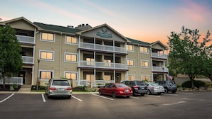 Ett hotell med flera våningar, en balkong på varje våning, en parkeringsplats med flera bilar och en amerikansk flagga på höger sida.