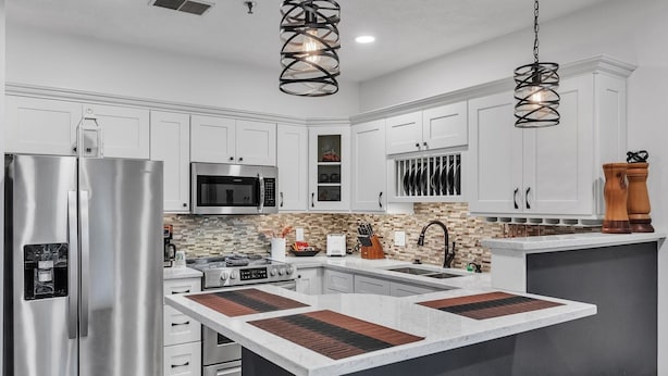 Una cocina moderna con armarios blancos, electrodomésticos de acero inoxidable, una isla central e iluminación colgante.