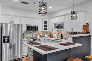 A modern kitchen with white cabinets, stainless steel appliances, a central island, and pendant lighting. - 2nd Floor Front Side Signature Suite - 201 by Grand Wood Suites (Nashville)