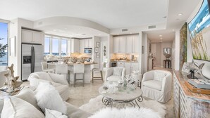 A spacious living area with a large white sofa, a coffee table, and a view of the kitchen. - Lagoon Tower 1301 3 Bedroom Condo (Gulf Shores)