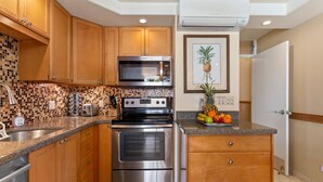A kitchen with wooden cabinets, a stainless steel stove, a microwave, and a tiled backsplash. - Mana Kai Maui Resort, #405a 1 Bedroom Condo (Kihei)