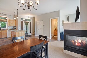 A spacious living room with a fireplace, a dining area with a wooden table and chairs, and a kitchen with wooden cabinets and a large window. - Present Pheasant 2 Bedroom Home (Redmond)