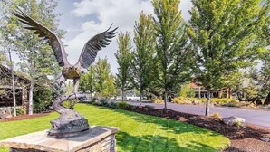 A landscaped area with a stone pedestal featuring a bird sculpture, surrounded by well-maintained grass and trees. - Present Pheasant 2 Bedroom Home (Redmond)