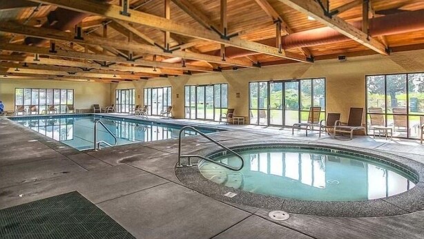 A large indoor swimming pool with a hot tub, wooden beams, and large windows. - Present Pheasant 2 Bedroom Home (Redmond)