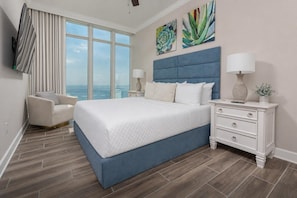 A bedroom with a large bed, a chair, a nightstand, and artwork on the wall. - Phoenix Gulf Towers 2704 4 Bedroom Condo (Orange Beach)