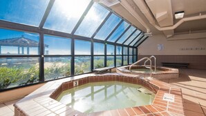 Una piscina en la azotea con cerramiento de vidrio, un jacuzzi y vistas a un edificio lejano.