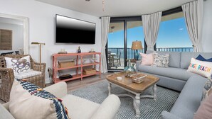 Un salón espacioso con un televisor de pantalla plana grande, un sofá cómodo, un sillón de mimbre y una mesa de centro de madera.