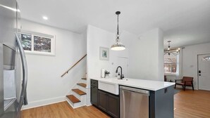 A modern kitchen with a central island, stainless steel appliances, and a wooden staircase.
