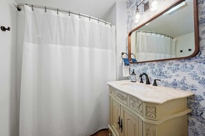 A bathroom with a white shower curtain, a sink with a mirror, and patterned wallpaper. - Morrill Modern Retreat – Desirable Marion Village! (Columbus)