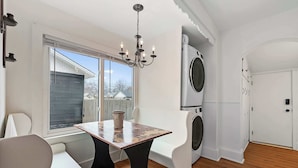 A modern kitchen with a built-in washer and dryer, a dining area with a table and chairs, and a large window providing a view of the outside.