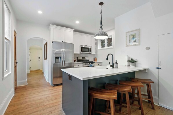 A modern kitchen with white cabinetry, stainless steel appliances, a central island with stools, and a pendant light. - Morrill Modern Retreat – Desirable Marion Village! (Columbus)