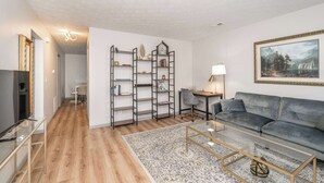 A modern living room with a grey sofa, a coffee table, a bookshelf, and a painting on the wall. - Arkstone Retreat 1 - 4 minutes from the Ark! (Williamstown)