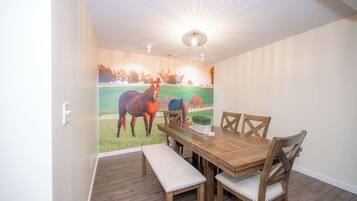 Un comedor con mesa de madera, bancos acolchados y un mural de caballos en la pared.