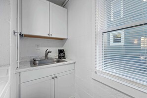 A compact kitchen with white cabinets, a stainless steel sink, and a coffee maker.