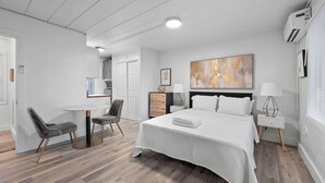 A modern hotel room with a large bed, a desk, two chairs, a bedside table with a lamp, and a large abstract painting on the wall. - Chic City Retreat 93E (Columbus)