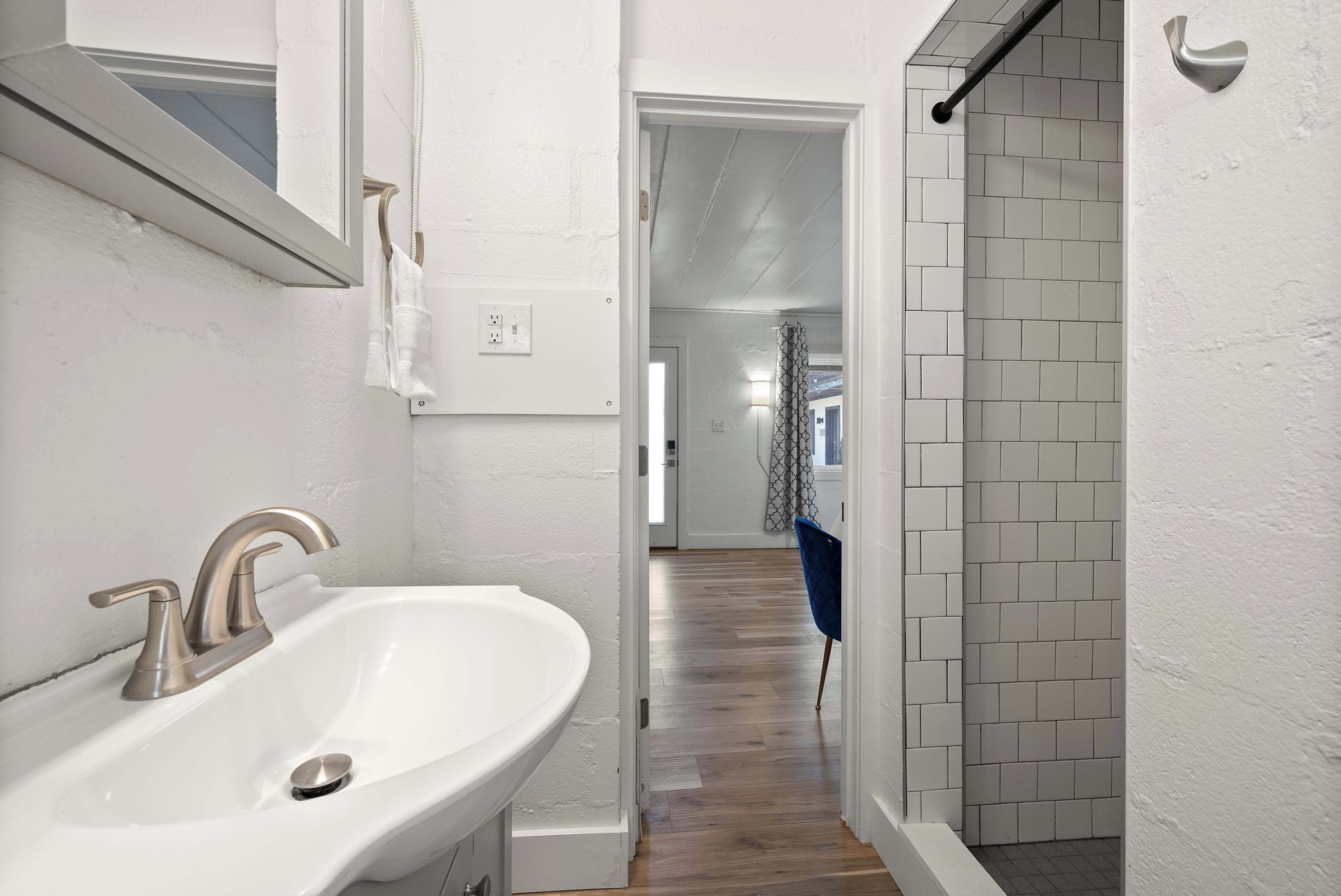 A bathroom with a white sink, a mirror, and a shower area with tiled walls.