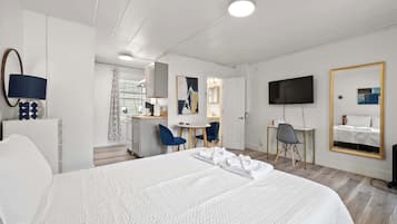 A hotel room with a large bed, a desk, two chairs, a TV, and a mirror.