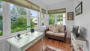 A room with a green desk, a wicker sofa, and a television on a cabinet. - Classic Charm on Ashland – For 8 (Columbus)