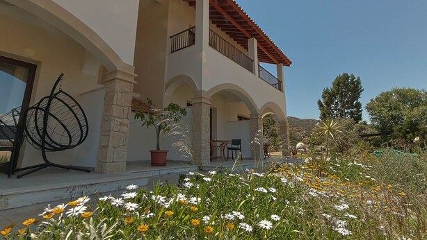 Un edificio de dos pisos con balcón, pilares de piedra y un jardín lleno de flores.