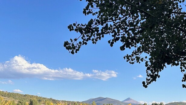 A lakeside view with a bench and table, surrounded by autumn foliage and distant mountains.