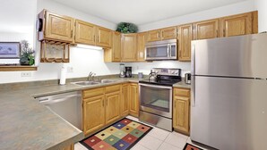 A modern kitchen with wooden cabinets, stainless steel appliances, and a colorful rug.