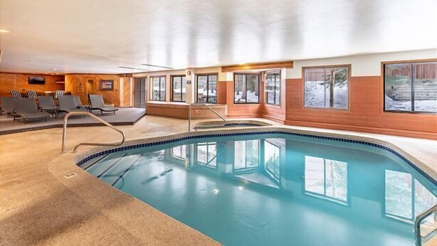 An indoor swimming pool with a clear view of the surrounding area, including a seating area with chairs and a wooden wall.