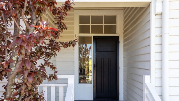 A front porch with a black door, white railings, and a doormat. - Hollybrooke Cottage, prestige suburb in Launceston (East Launceston)